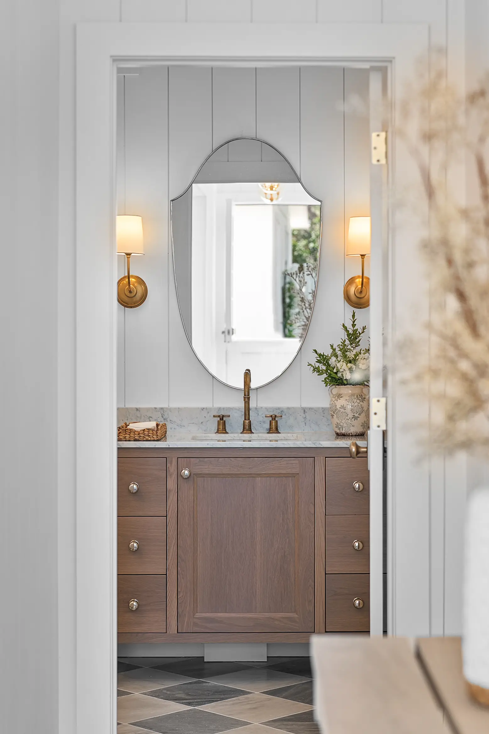 Powder room with a wood vanity, arched mirror and brass sconces