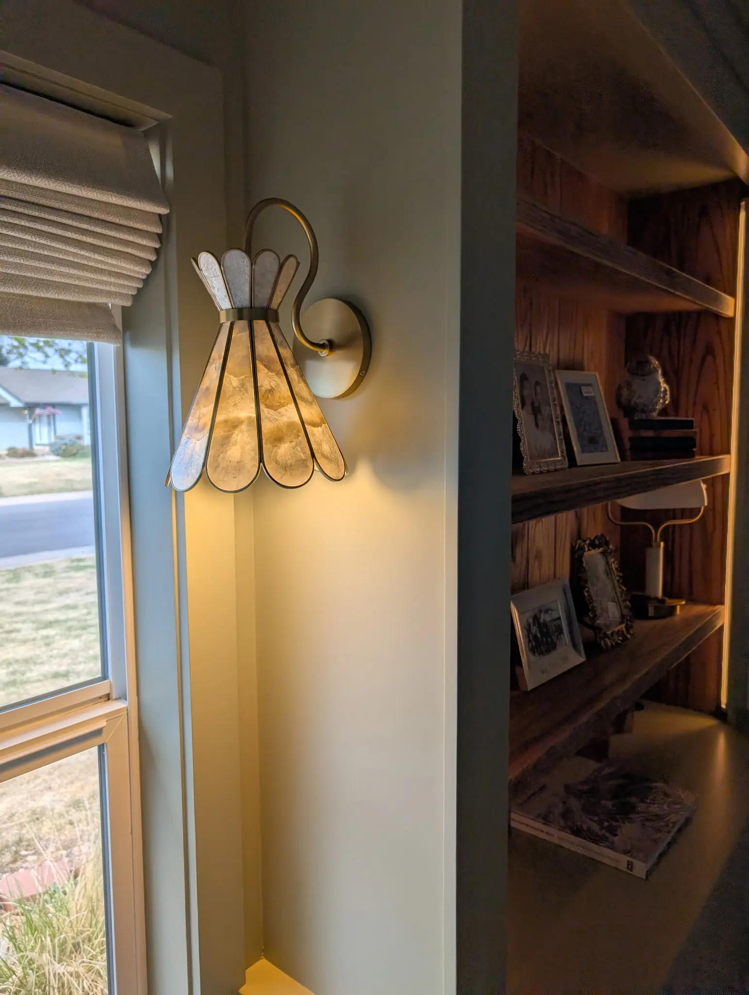 Built-in shelving with interior lighting beside a window and wall sconce