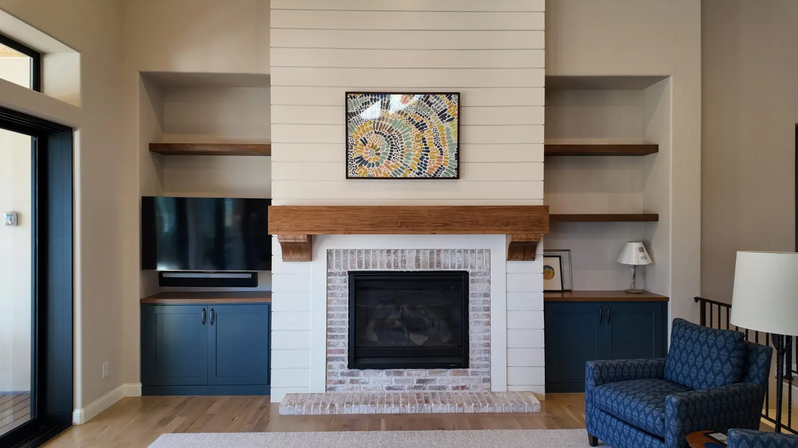 Shiplap fireplace wall with a wood mantel, open shelving and blue lower cabinets