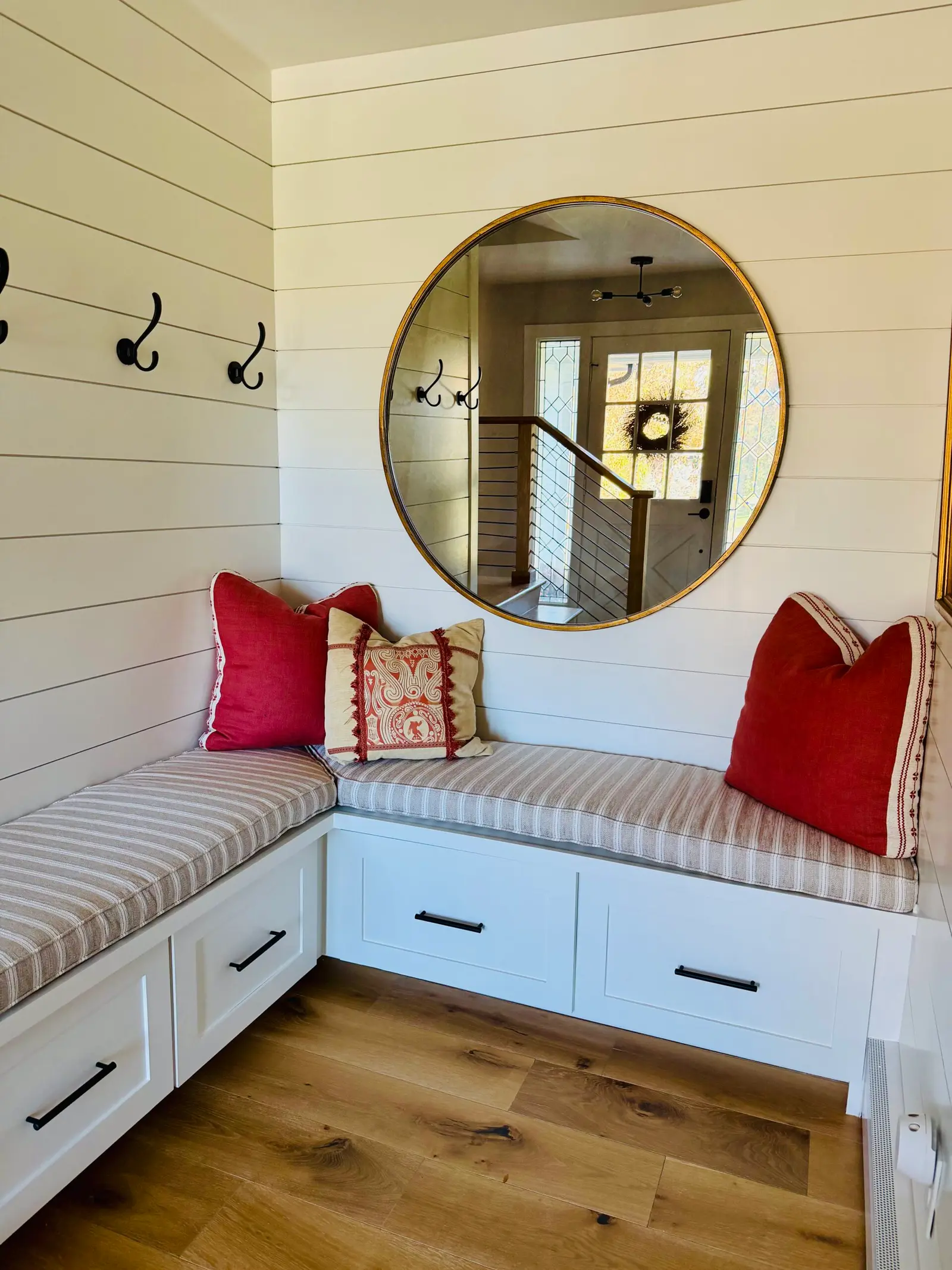 Mudroom bench nook with shiplap walls, coat hooks and a round mirror