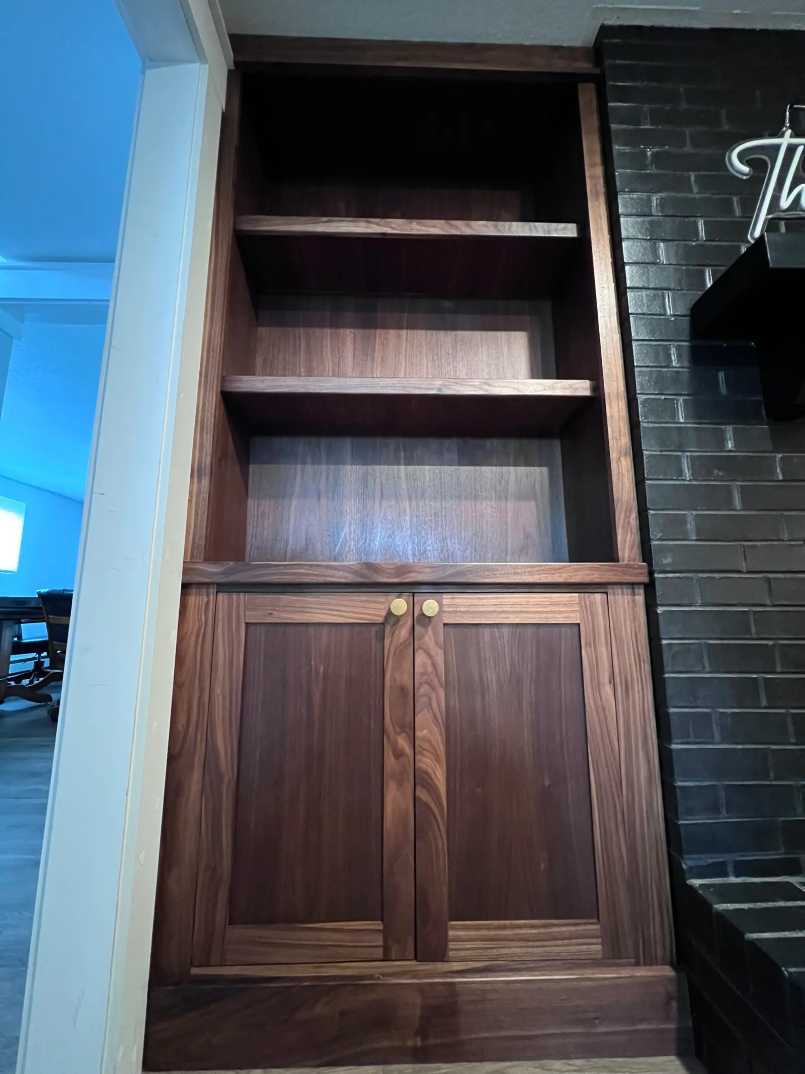 Dark wood built-in cabinet and shelves beside a black brick wall
