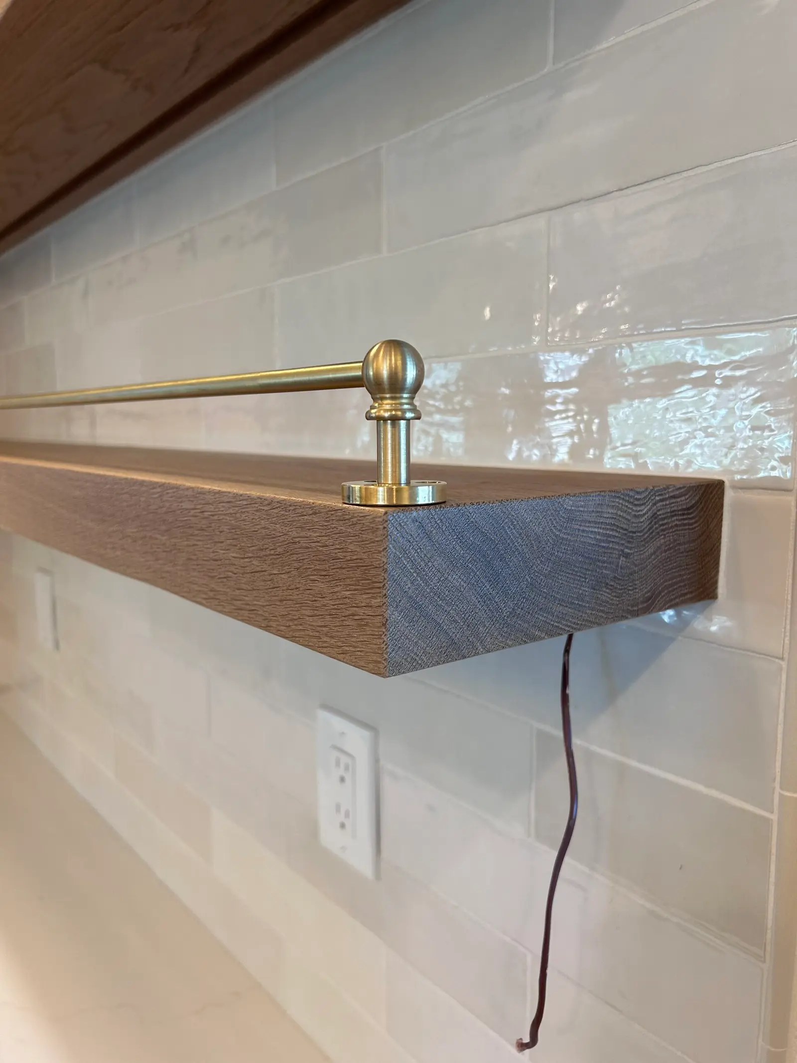 Dark floating shelf with a brass rail in a tiled kitchen
