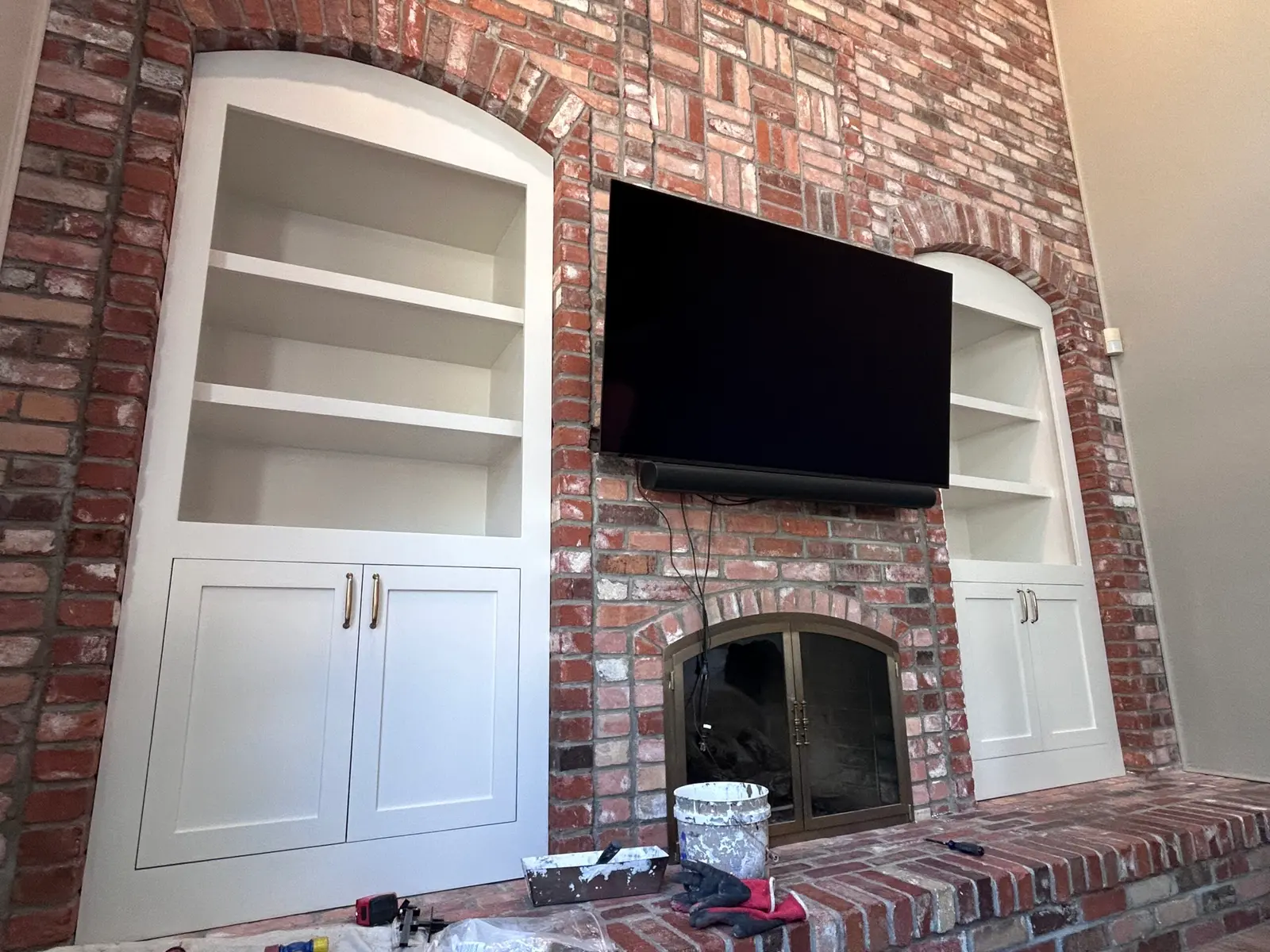 White arched built-in cabinets on both sides of a brick fireplace