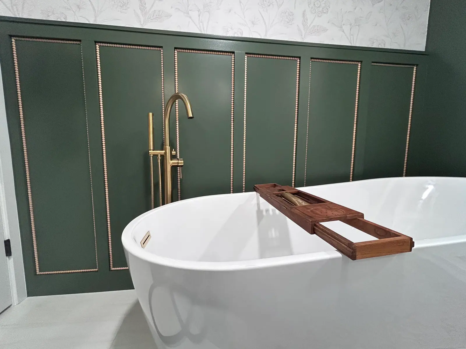 Green paneled bathroom wall behind a freestanding tub with a wood bath tray
