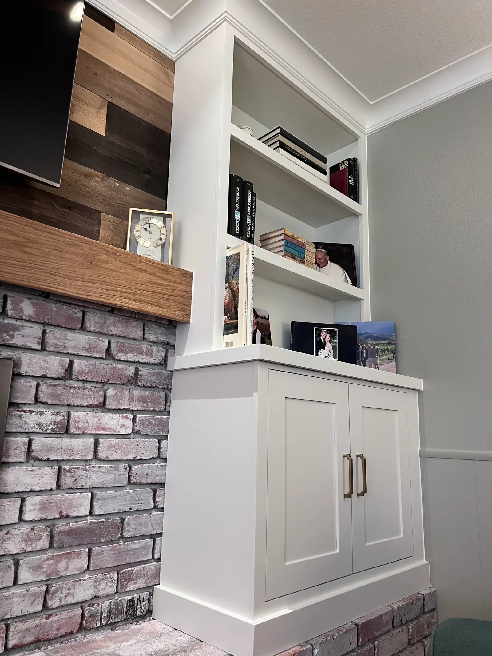 White built-in bookcase and cabinet beside a brick fireplace with a wood mantel