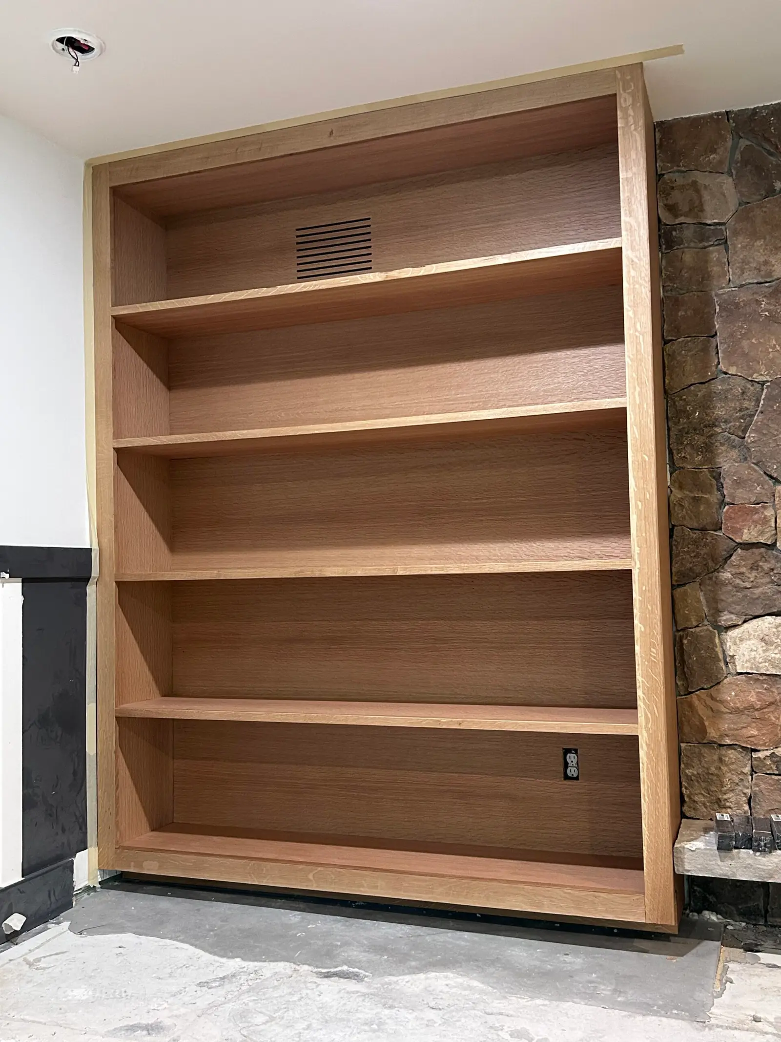 Freestanding wood bookcase beside a stone wall
