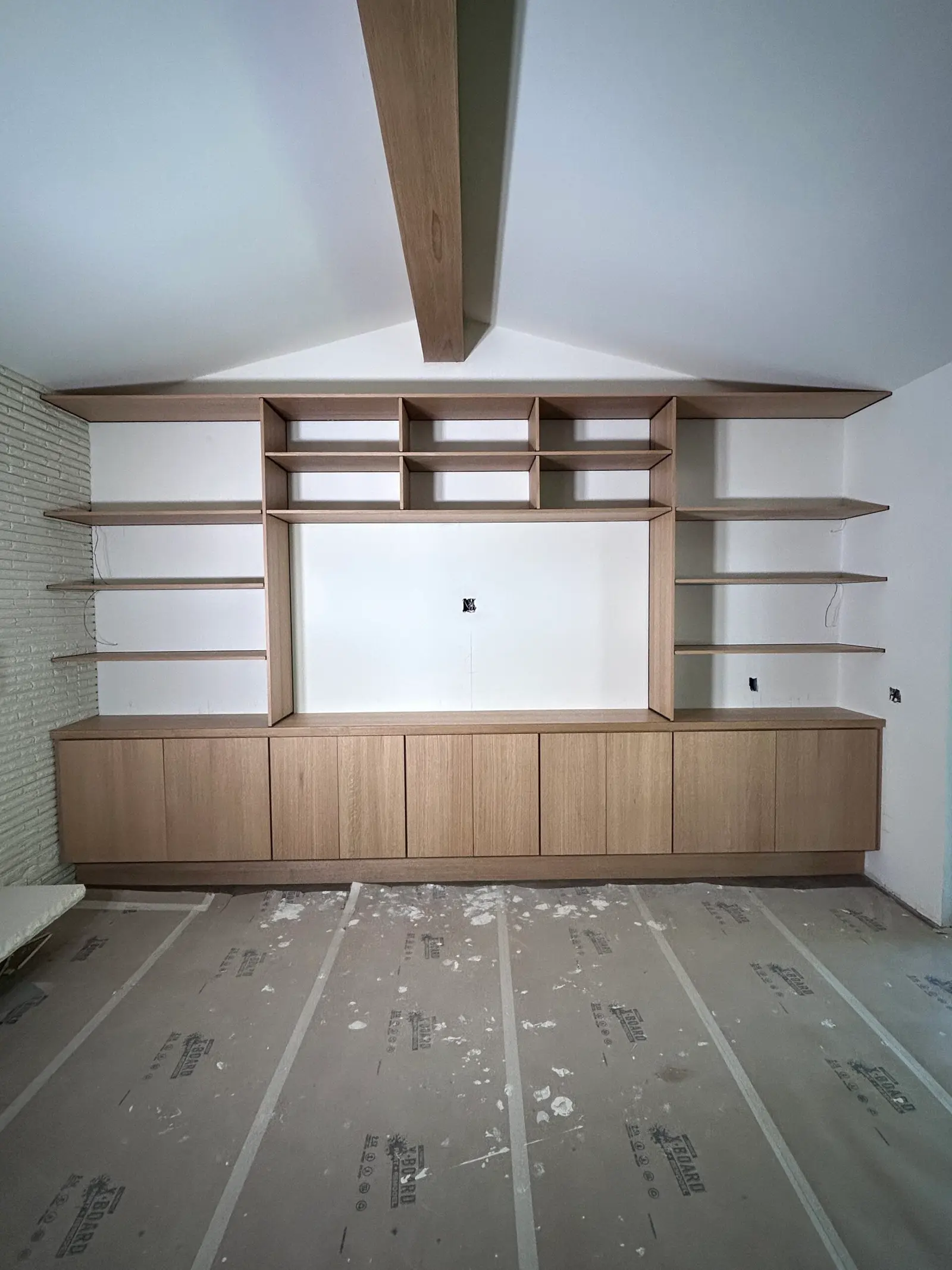 Light wood built-in entertainment wall with floating shelves during installation