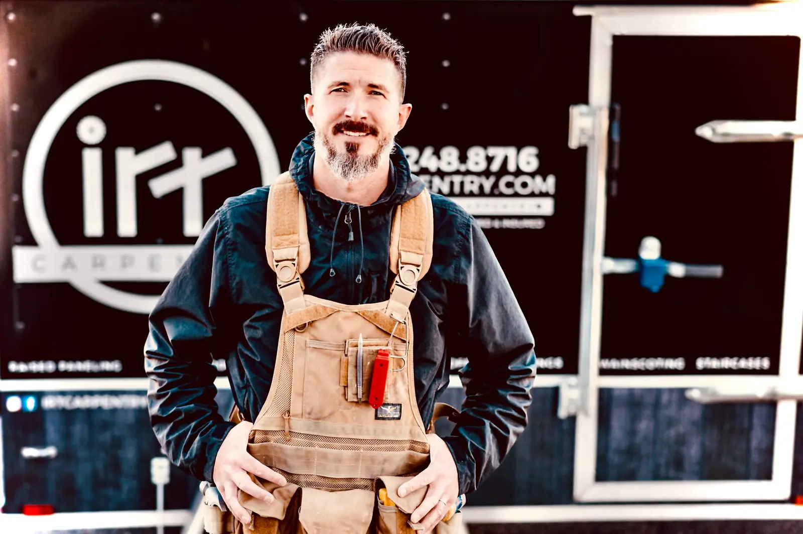 Dan Hall, founder of IRT Carpentry, in work overalls in front of the IRT Carpentry trailer