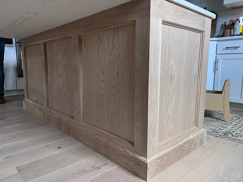 Kitchen island wrapped in light wood raised panels